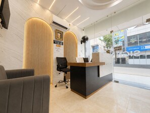 A reception area with a modern design, featuring a reception desk, seating area, and a large window offering a view of the street. - Hotel Signature INN (Vrindavan)