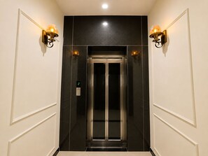 An elevator with a digital display showing the number 2, flanked by wall sconces with light bulbs. - Hotel Signature INN (Vrindavan)