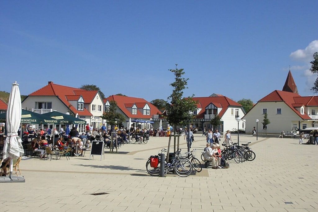 Ein öffentlicher Platz mit Gebäuden, Sitzgelegenheiten im Freien und Fahrrädern.