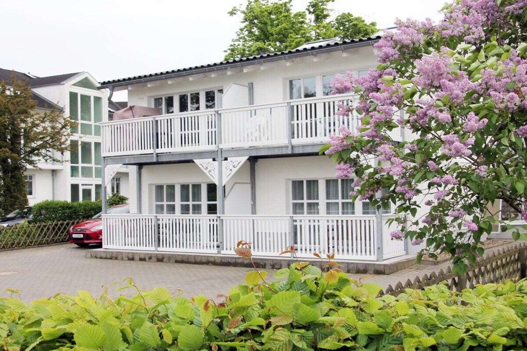 A two-story residential building with balconies, a driveway, and a red car parked in front.