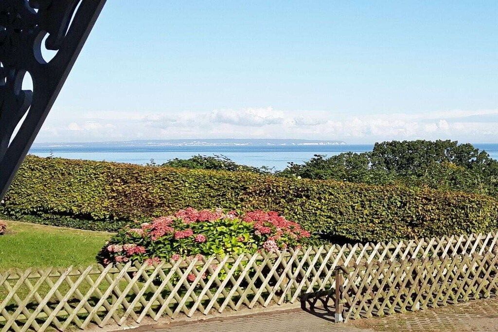 A view of a garden with a wooden fence, a bench, and a body of water in the distance.