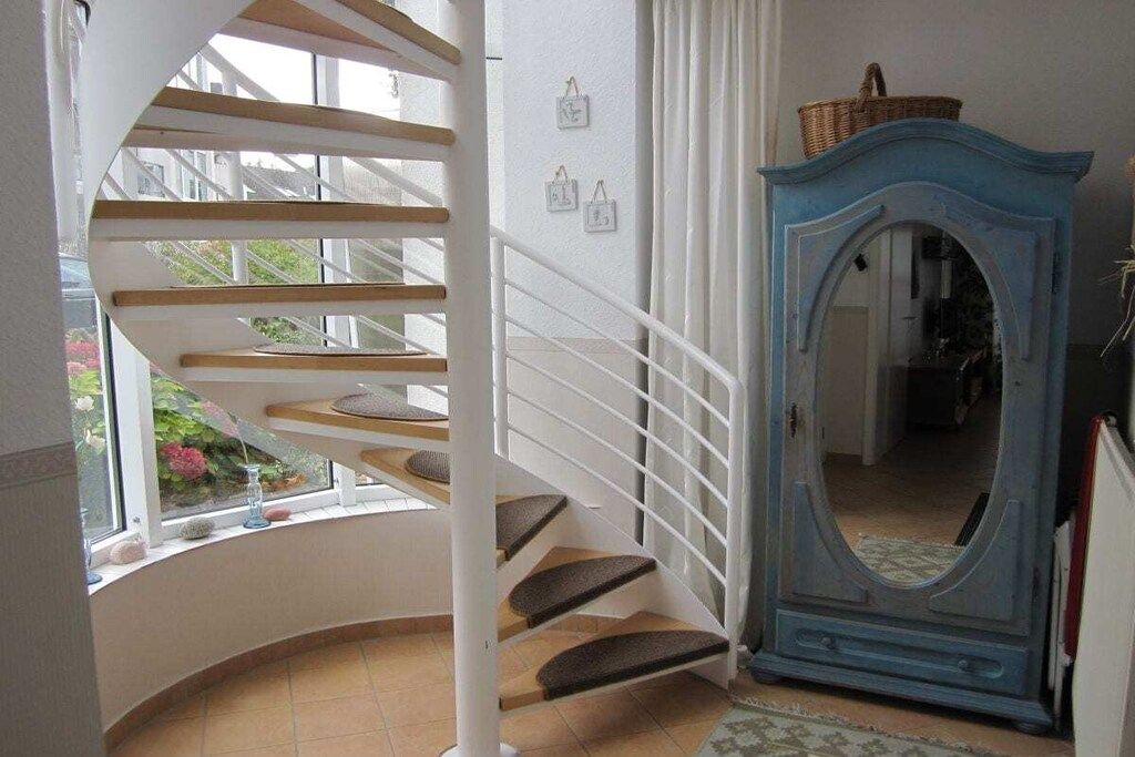 A spiral staircase with a white railing, a blue cabinet with a mirror, and a window with a view of greenery.
