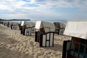 Strandhütten mit weißen Markisen, in Reih und Glied an einem Sandstrand aufgestellt, mit Blick auf das Meer.