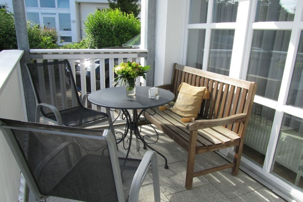 A balcony with a wooden bench, a round table, and two chairs.