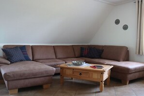 Ein Wohnzimmer mit einem braunen Ecksofa, einem Holztisch und zwei Wanduhren.
