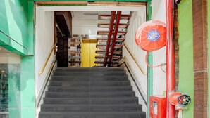 En trappe fører op til en gul dør, med en rød brandslange og brandslukker til højre.