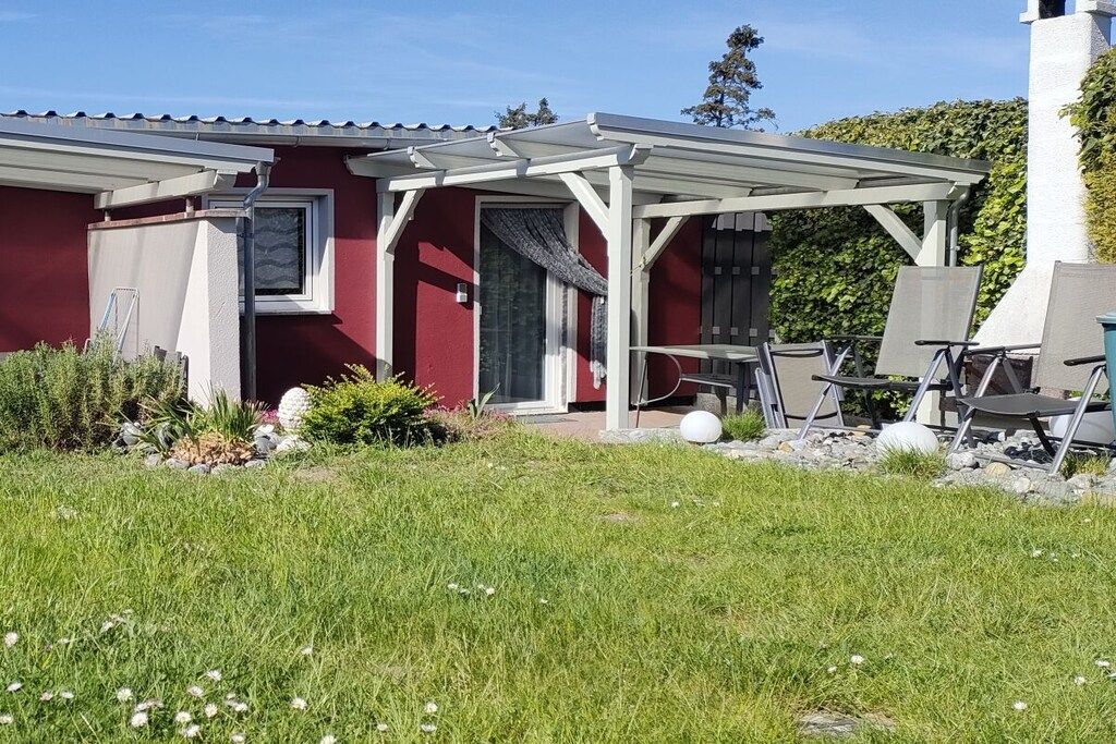 A red building with a covered patio area, outdoor seating, and a grassy lawn.