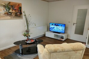 A living room with a flat-screen TV on a white stand, a round black coffee table with a vase of flowers, and a beige sofa. - Holiday apartment in Gager with swimming pool (Gager)