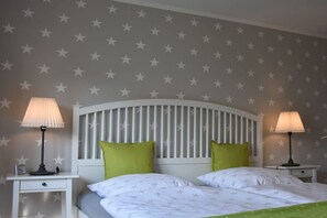 Ein Schlafzimmer mit einer Wand im Sterne-Muster, einem weißen Kopfteil, zwei Nachttischen mit Lampen und grünen Kissen.