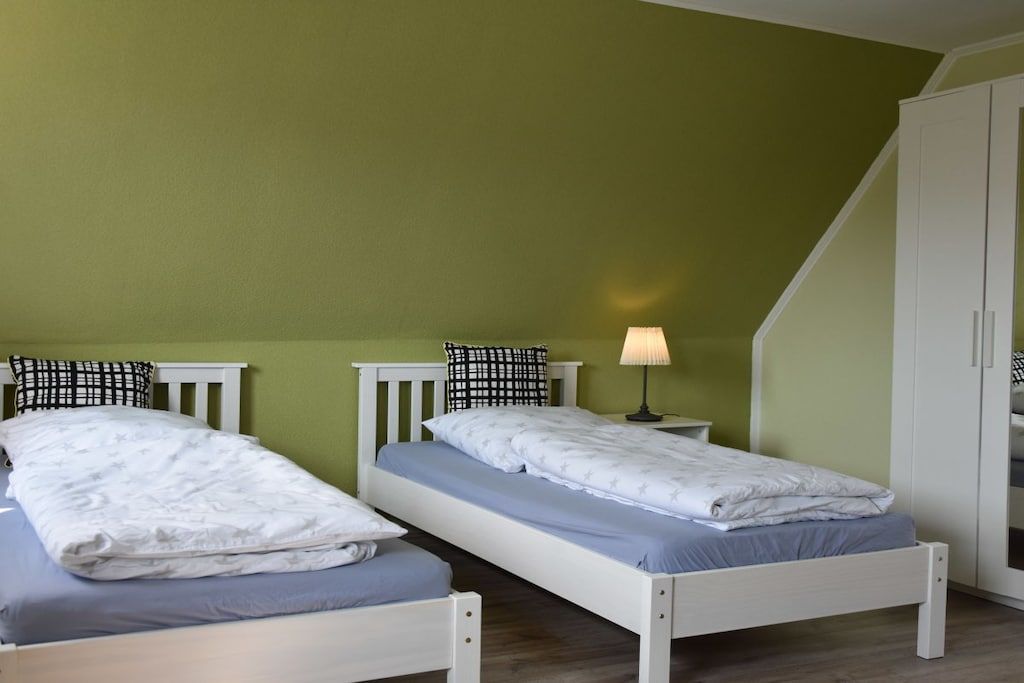Una habitación con dos camas individuales, una mesita de noche con lámpara y un armario.