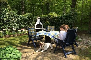 An outdoor dining area with a grill, chairs, and a dog. - Wendt Forestry House "Waldblick" (Timmendorfer Strand)