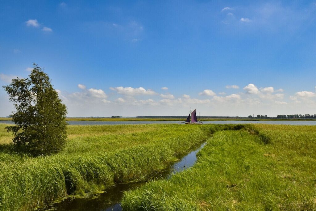 A grassy landscape with a small water channel and a sailboat in the distance.