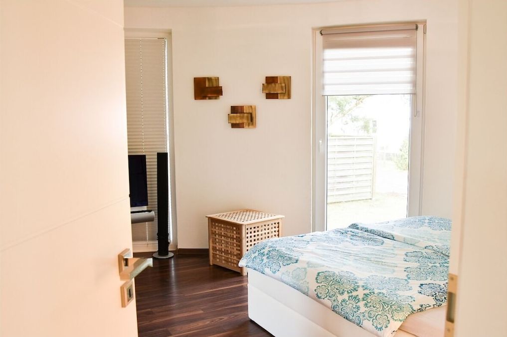 A bedroom with a bed, a window, a door, and a small wooden stool.