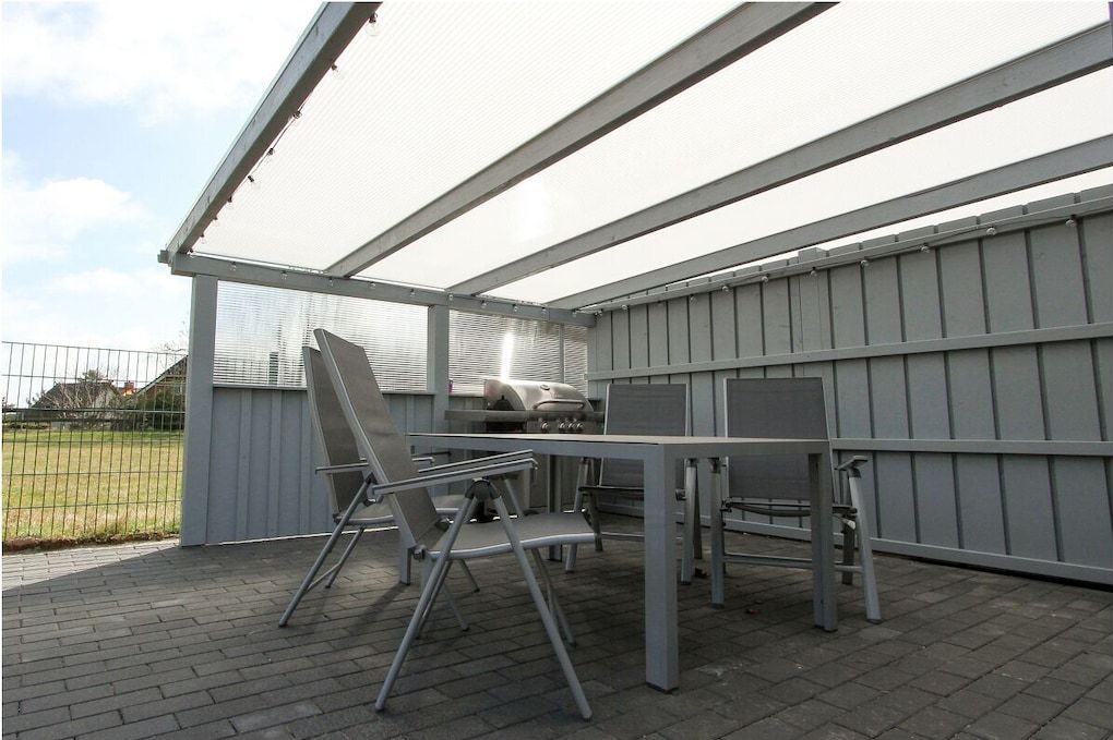 Un patio exterior con una parrilla, sillas de metal y una mesa.