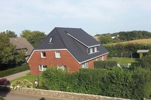 A two-story house with a sloped roof, surrounded by a well-maintained garden and hedges. - Holiday apartment with 2 bedrooms (Borgsum auf Föhr)