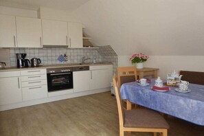 A compact kitchen with white cabinets, a built-in oven, and a dining area with a table set for tea. - Holiday apartment with 2 bedrooms (Borgsum auf Föhr)