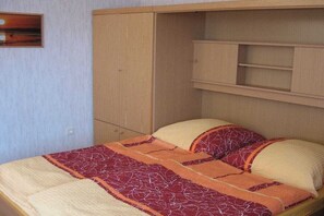 A single bed with a patterned bedspread and pillows, a wooden wardrobe, and a shelf unit. - Holiday apartment with 2 bedrooms (Borgsum auf Föhr)