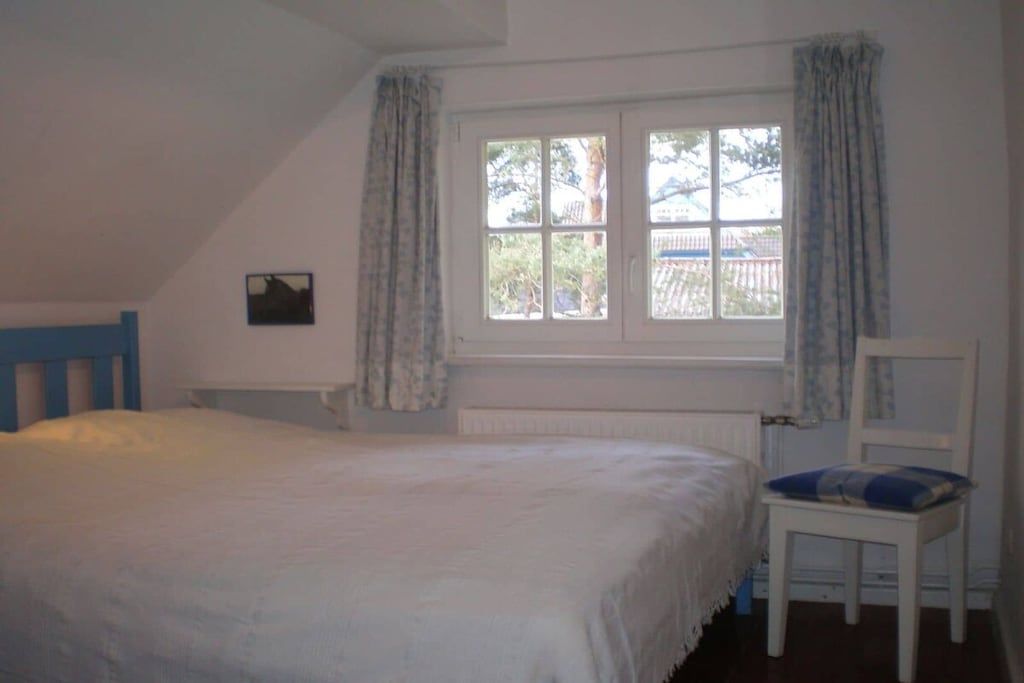 Un dormitorio con cama, una silla, ventana con cortinas y radiador.
