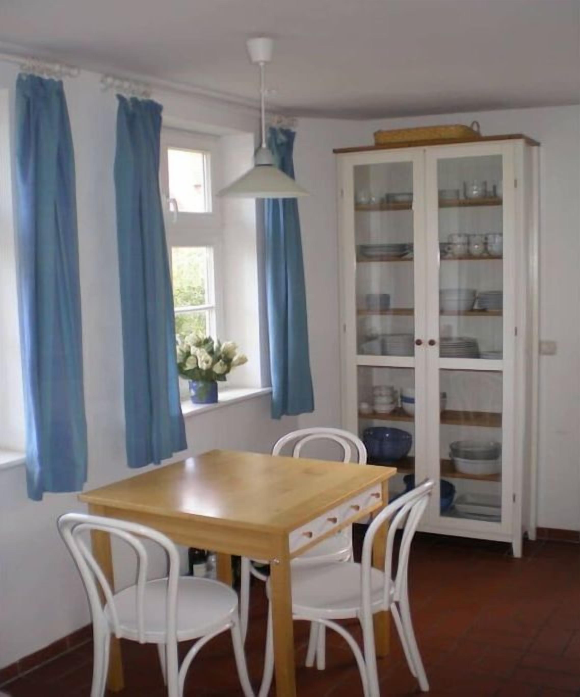 A dining area with a wooden table and white chairs, a cabinet with glass doors, and blue curtains.