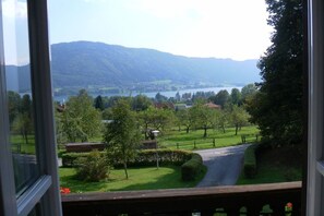 A view from a window overlooking a green landscape with a lake and mountains in the distance. - Landhaus Arztmann - Fewo Linde (Bodensdorf am Ossiacher See)