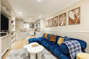 A living room with a blue sofa, white coffee table, and a television. There are framed botanical prints on the wall. - New! 2BR Garden Flat by Victoria Park (Greater London)
