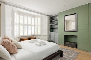 A bedroom with a large bed, a bay window, a green wall, a fireplace, and a mirror. - New! 2BR Garden Flat by Victoria Park (Greater London)