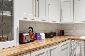 A kitchen with white cabinets, a wooden countertop, a toaster, a kettle, and a coffee maker. - New! 2BR Garden Flat by Victoria Park (Greater London)