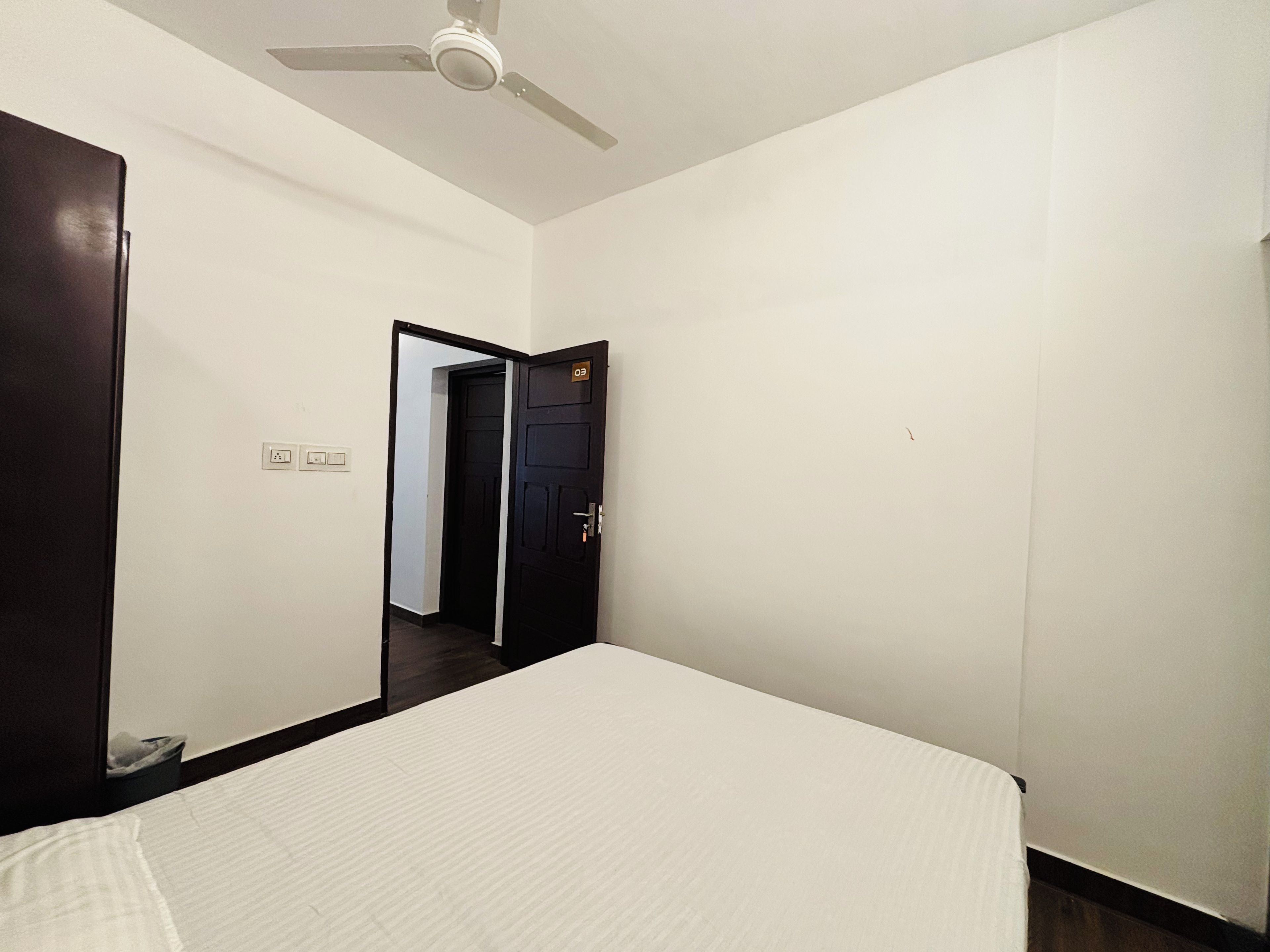 A bedroom with a bed, a ceiling fan, a door, and a light switch.