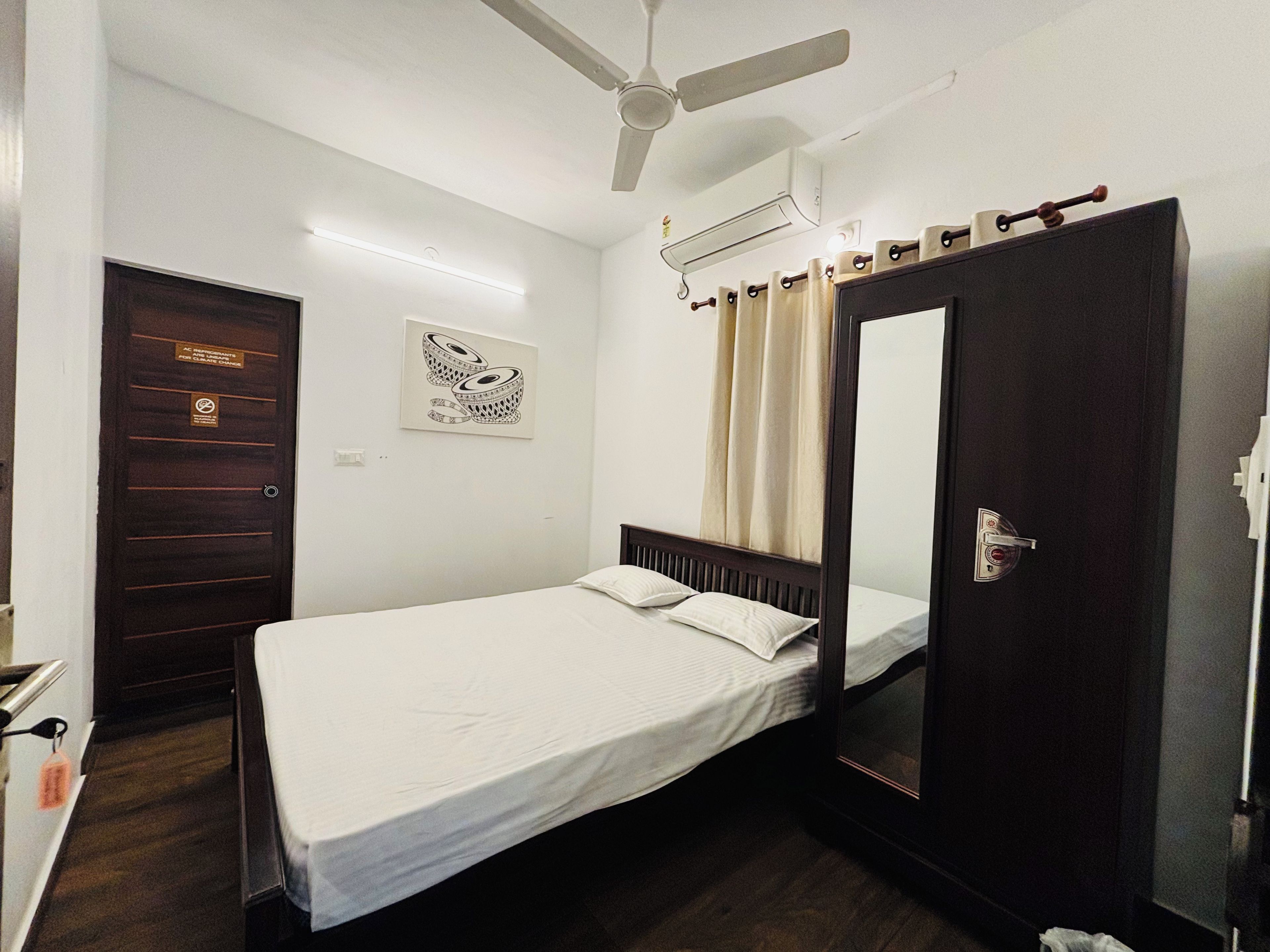 Una cama individual con cabecera de madera, ventilador de techo, aire acondicionado, una puerta con espejo y una obra de arte colgada en la pared.