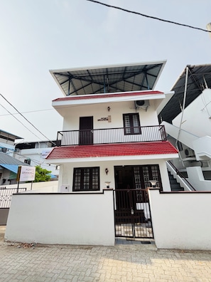 A two-story building with a flat roof, a balcony, and a gated entrance. - Fort Grande INN (Kochi)