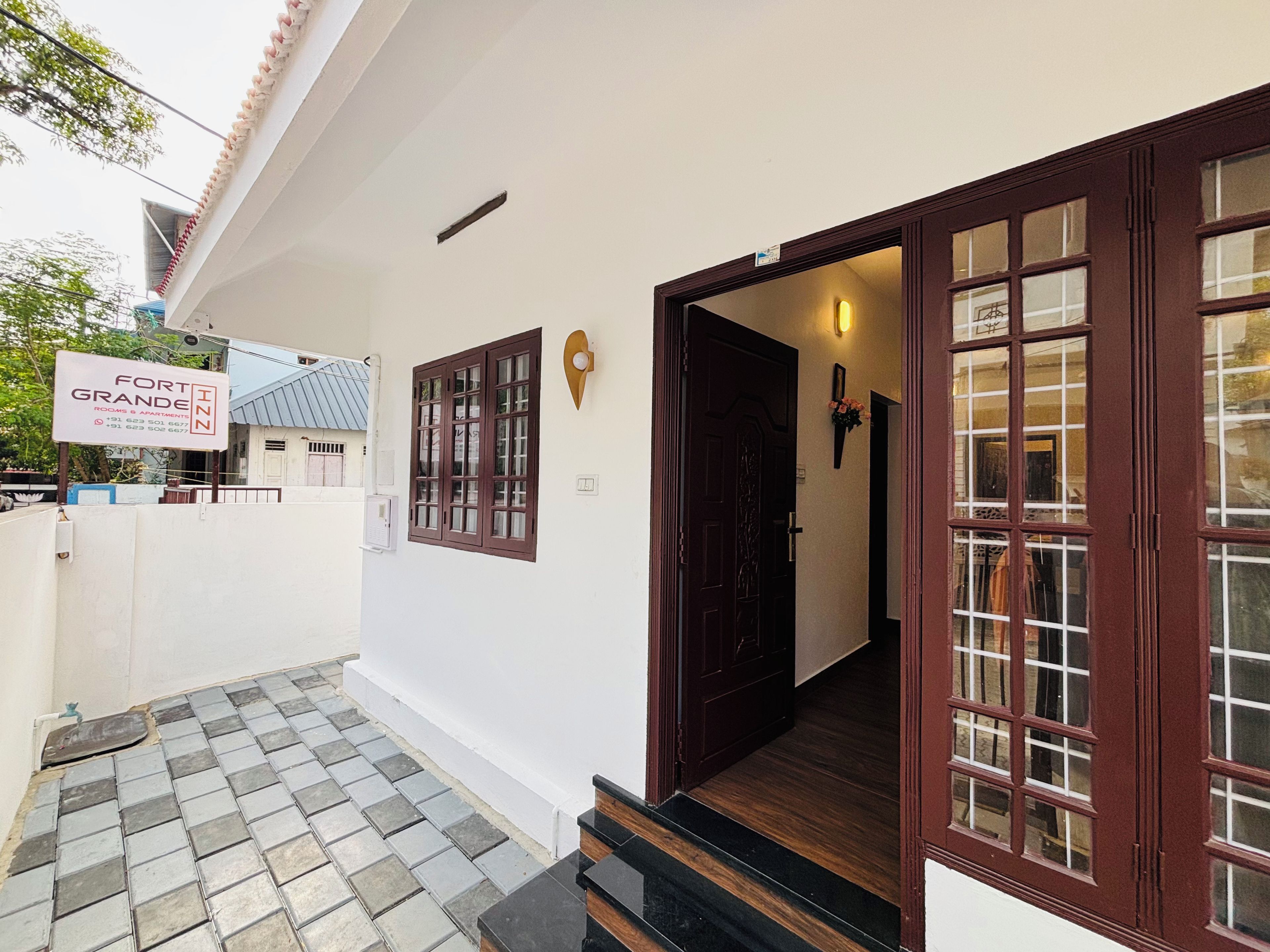 A hotel entrance with a signboard, a wooden door, and a tiled pathway leading to the entrance.