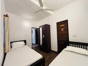 Habitació d'hotel amb dos llits, un ventilador de sostre, un armari i una porta amb un cartell.