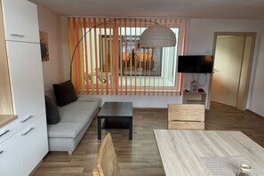 A modern living room with a sofa, a coffee table, and a TV. There is a balcony with a view of the outside. - Holiday apartment with 2 bedrooms (Dorfgastein)