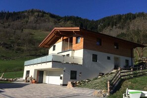 Ein zweistöckiges Gebäude mit Balkon, Garage und einer Treppe, die zu einer Holzterrasse führt.