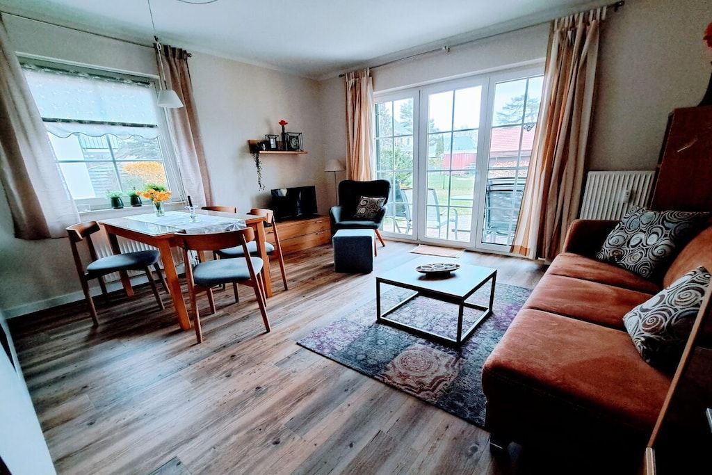 Ett vardagsrum med trägolv, en soffa, ett soffbord, ett matbord med stolar och en tv.