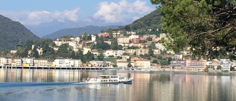 Un lac paisible avec un bateau, des bâtiments sur la rive et des collines en arrière-plan.