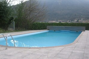 Ein rechteckiger Pool mit einer Metallleiter an einer Seite, umgeben von einer gepflasterten Terrasse.