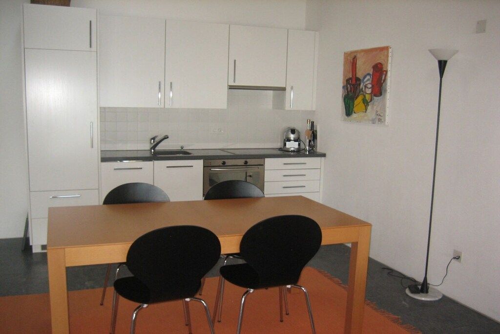 A compact kitchen with white cabinets, a wooden table, and two black chairs.