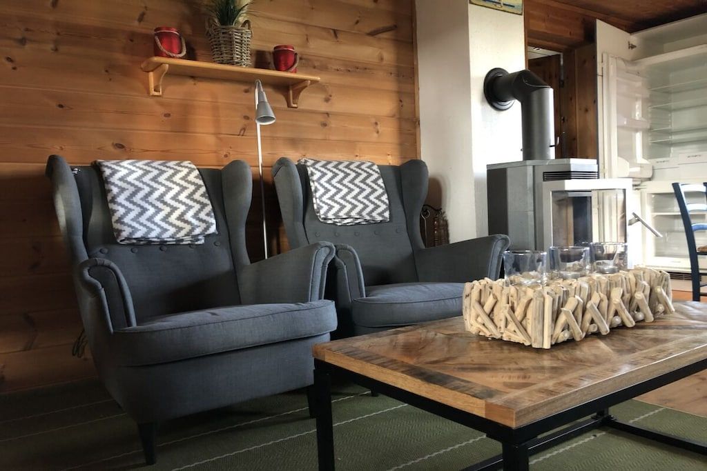 Une pièce comprenant deux fauteuils gris, une table basse en bois agrémentée d’un élément décoratif, une cheminée et une étagère avec divers objets.