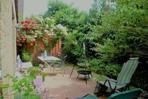 Eine Terrasse mit Tisch und Stühlen, umgeben von üppiger Bepflanzung und blühenden Pflanzen.