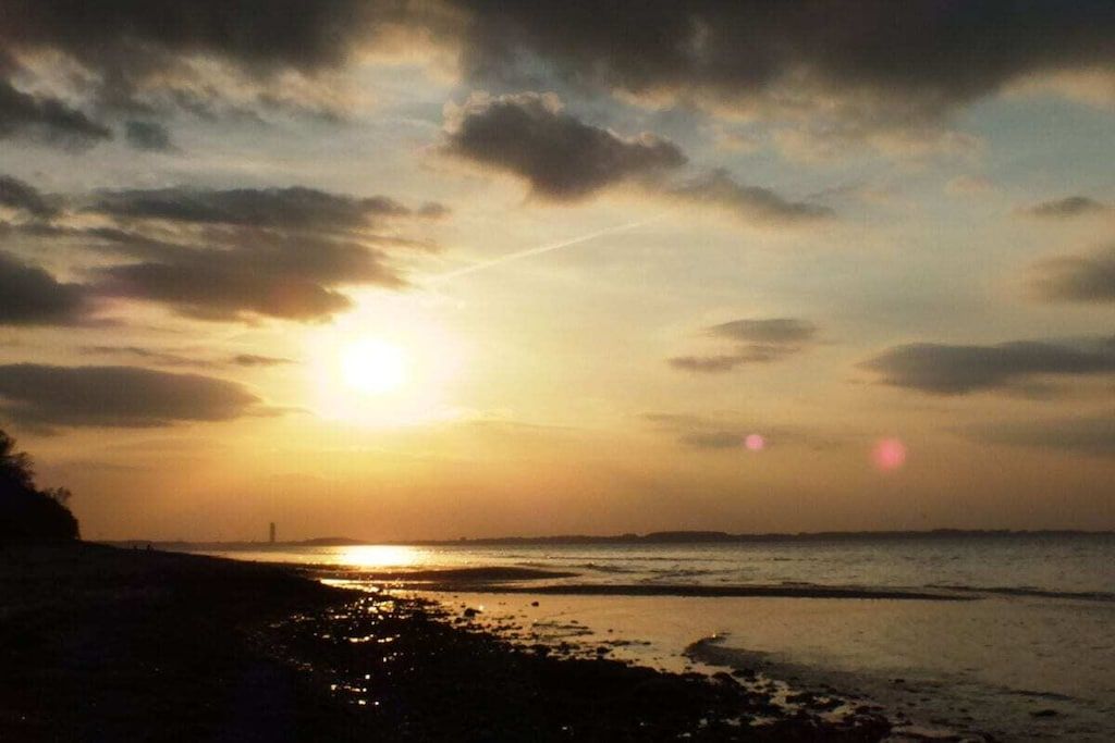 Ein Sonnenuntergang über einem Strand mit einem fernen Leuchtturm.