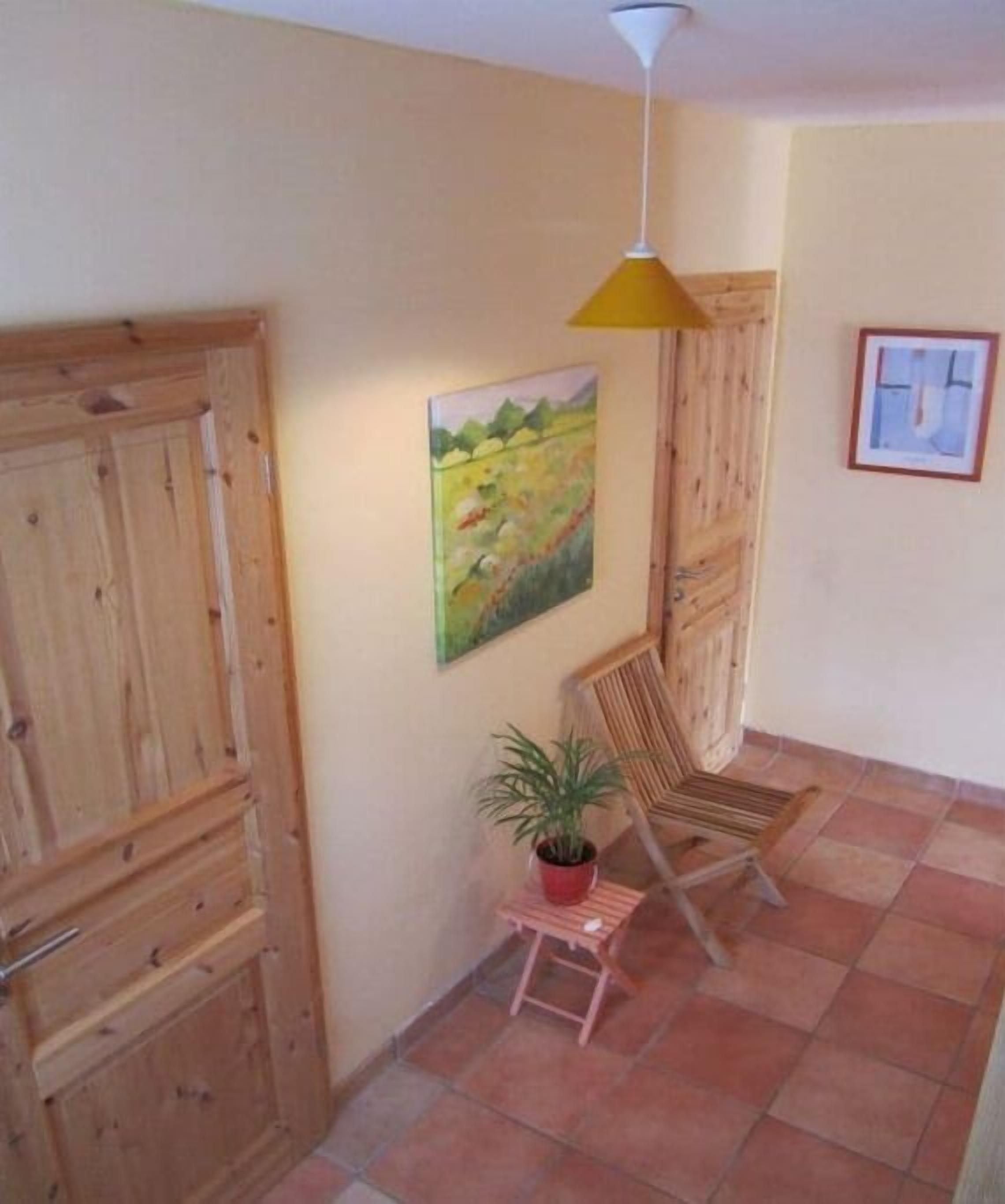 Ein Zimmer mit Holzausstattung, einem Gemälde, einem Sessel, einer Topfpflanze und einer Pendelleuchte.