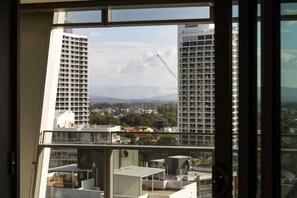 A view from a window overlooking a cityscape with multiple high-rise buildings, a construction crane, and a distant mountain range. - Westlight by Aryve | Surfers Paradise (Surfers Paradise)
