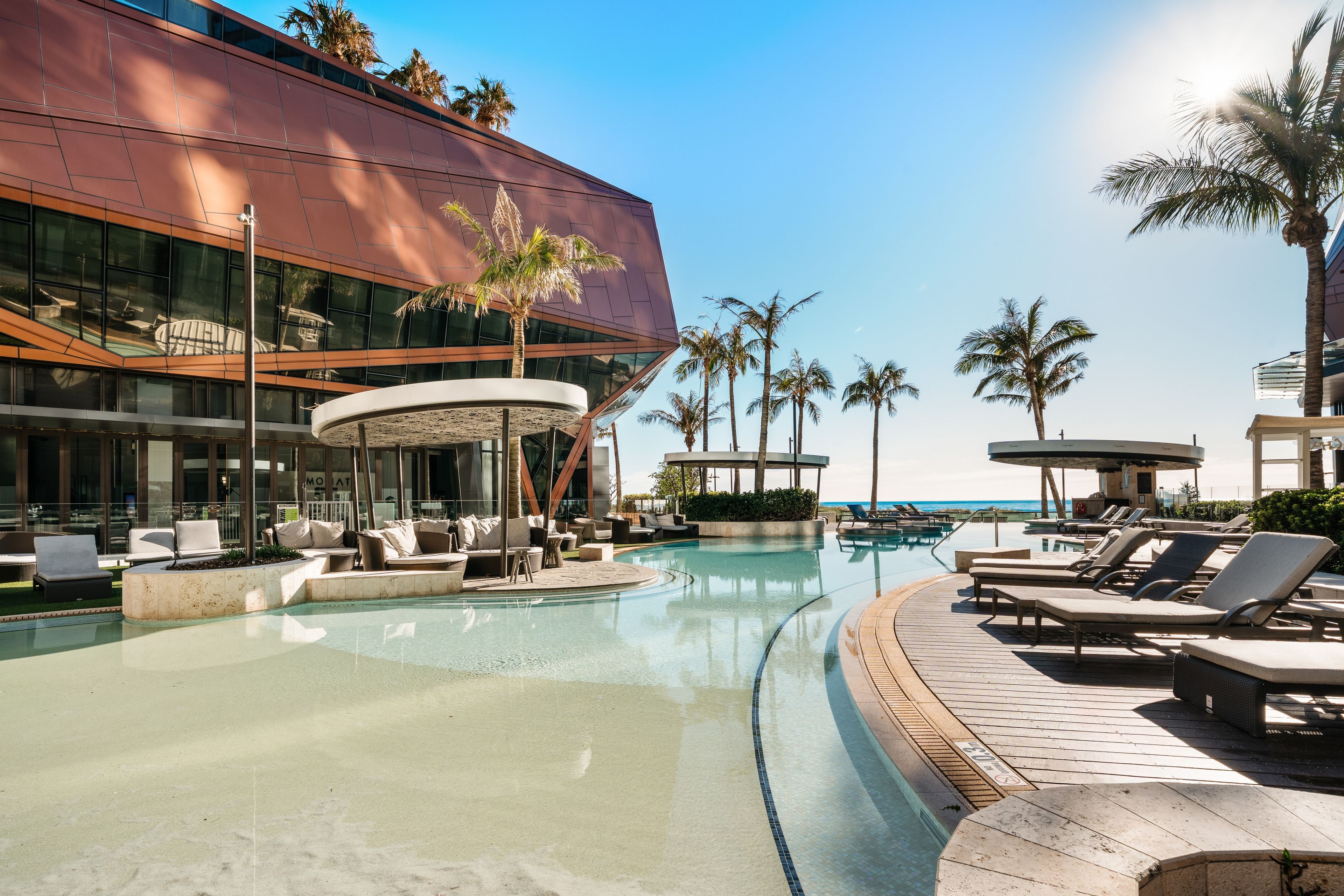A modern hotel with a pool area, lounge chairs, and palm trees.