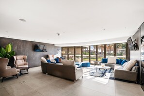 Un salon moderne doté d’un téléviseur à écran plat, de sièges confortables et de grandes fenêtres offrant une vue sur l’extérieur.