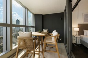 A hotel room with a large window, a bed, a bedside table with a lamp, and a small table with chairs. - Westlight by Aryve | Surfers Paradise (Surfers Paradise)