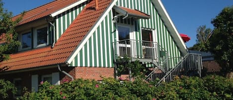 Une maison à deux étages avec un toit recouvert de tuiles rouges, des murs à rayures vertes et blanches et un balcon doté d’une balustrade en métal.
