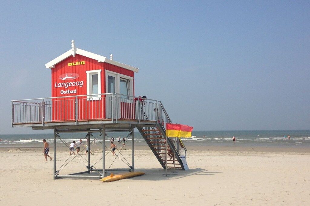 A lifeguard tower with a red and white color scheme, a staircase leading to the top, and a flag on the side.