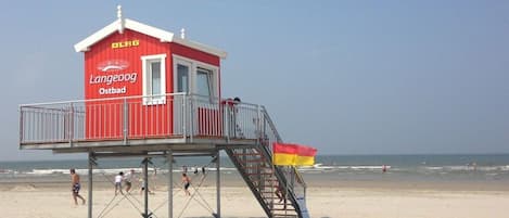 A lifeguard tower with a red and white color scheme, a staircase leading to the top, and a flag on the side.