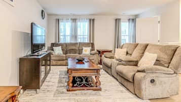 A living room with a sofa, a coffee table, a TV, and a clock on the wall.